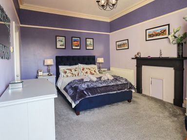 A bedroom with a bed bedside tables lamps framed pictures a fireplace and a dresser at Gale Lodge Cottage Ambleside