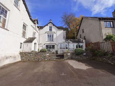 The exterior of a white house with stone walls and a gated patio area in front with parking spaces at Gale Lodge Cottage in Ambleside