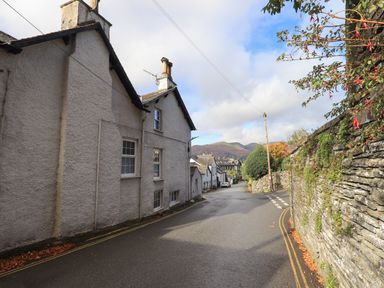 A narrow street with white houses on the left and a stone wall with greenery on the right at Gale Lodge Cottage in Ambleside