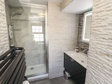 A bathroom with a glass shower enclosure a black heated towel rail and a sink with a mirror at Gale Lodge Cottage in Ambleside