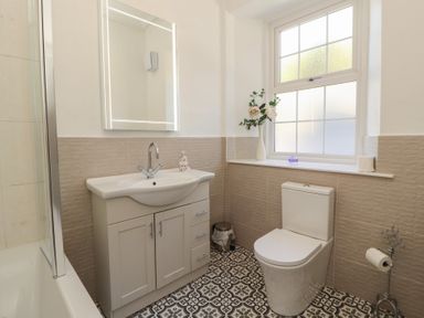 A bathroom with a sink cabinet toilet patterned floor and a window at Gale Lodge Cottage in Ambleside