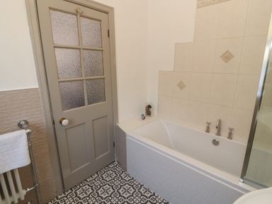 A bathroom with a bathtub towel radiator and a door at Gale Lodge Cottage Ambleside