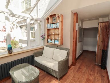 A small seating area with a wicker loveseat and glass coffee table near a window with bookshelves on the wall at Gale Lodge Cottage in Ambleside