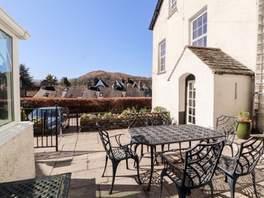 An outdoor patio with black metal table and chairs next to a white building at Gale Lodge Cottage in Ambleside