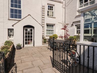 An outdoor patio area with a black metal table and chairs next to white buildings at Gale Lodge Cottage in Ambleside