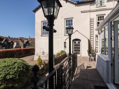 An outdoor patio with black metal lamps and railing beside a white building with windows and a door at Gale Lodge Cottage in Ambleside