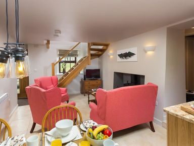 A living room with red armchairs a wooden staircase a dining table with food and drinks and a television at Barn Cottage in Bassenthwaite near Keswick