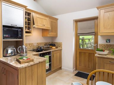 A kitchen with wooden cabinets toaster kettle microwave and a door at Barn Cottage in Bassenthwaite near Keswick