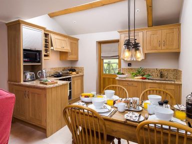 A kitchen with wooden cabinets dining table set with bowls cups and glasses at Barn Cottage in Bassenthwaite near Keswick