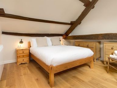 A bedroom with a wooden double bed with white bedding and pillows wooden furniture and exposed ceiling beams at Barn Cottage in Bassenthwaite near Keswick