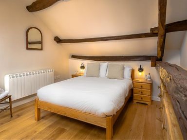 A bedroom with a wooden bed frame two bedside tables wooden beams on the ceiling and wooden floor at Barn Cottage in Bassenthwaite near Keswick