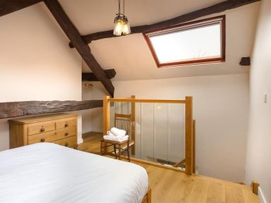 A bedroom with wooden beams a skylight a wooden dresser a wooden chair with towels and a bed at Barn Cottage Bassenthwaite near Keswick