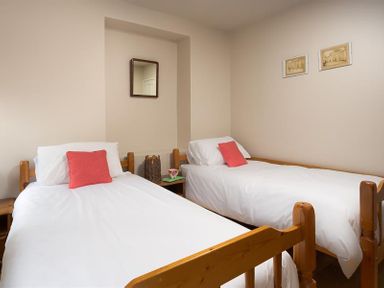 A bedroom with two single wooden beds with white bedding and red pillows at Barn Cottage in Bassenthwaite near Keswick