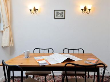 A wooden table with maps brochures and a mug with four black chairs and wall lights in a room at Mosslea in Bowness