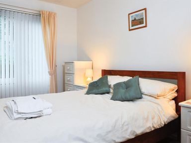 A bedroom with a double bed with white bedding and green pillows and bedside tables with lamps at Mosslea in Bowness