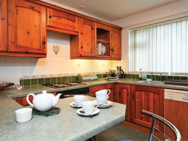 A kitchen with wooden cabinets white teapot and cups on the counter at Mosslea in Bowness