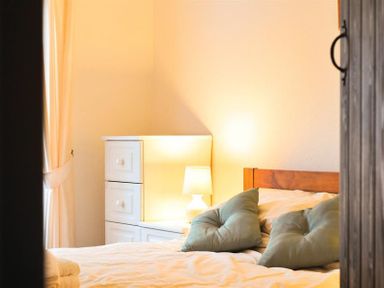 A bedroom with a wooden bed frame green pillows white dresser lamp and cream curtains at Mosslea in Bowness