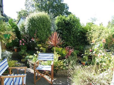 A garden with two striped chairs and various plants and shrubs surrounding a paved area at Mosslea in Bowness