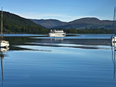 A lake with boats and a ferry with hills in the background at Mosslea in Bowness