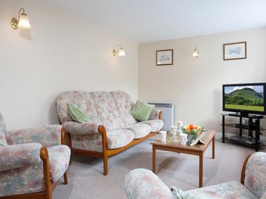 A living room with patterned sofas a wooden coffee table with cups and fruit bowl and a television at Low Croft Cottage in Grasmere