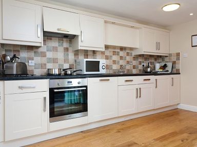 A kitchen with white cabinets a microwave stove oven kettle and cookware at Low Croft Cottage in Grasmere