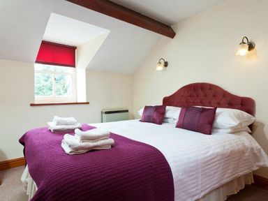 A bedroom with a double bed with purple bedspread and pillows and a window with a red blind at Low Croft Cottage in Grasmere