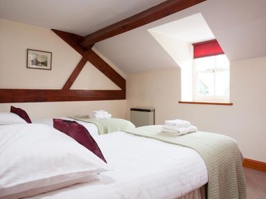 A bedroom with two single beds with white linens and red pillows under a window with a red blind at Low Croft Cottage in Grasmere