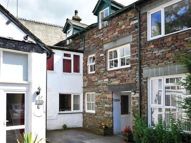 Exterior view of a stone and white plaster building with multiple windows and doors Low Croft Cottage Grasmere