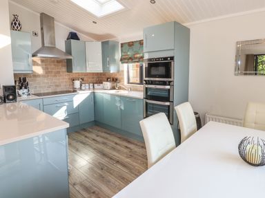 A kitchen with blue cabinets a white dining table with chairs and wooden flooring at Windermere Lodge in Bowness-On-Windermere