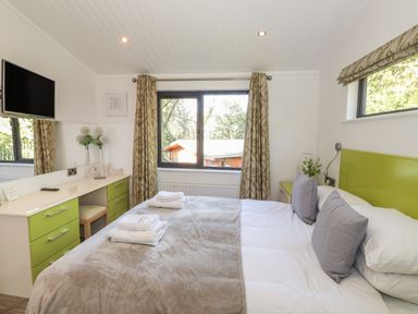 A bedroom with a bed towels on a blanket and a dresser with a TV and flowers at Windermere Lodge in Bowness-On-Windermere