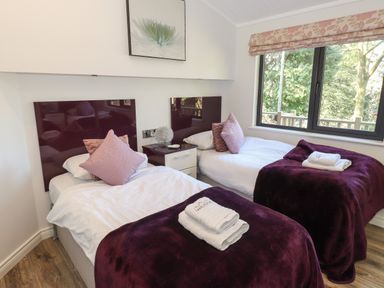 A bedroom with two single beds with purple blankets and pillows and a window with a view of trees at Windermere Lodge in Bowness-On-Windermere