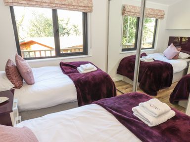 A bedroom with two single beds with purple throws and pillows next to a window and mirrored wardrobe at Windermere Lodge Bowness-On-Windermere