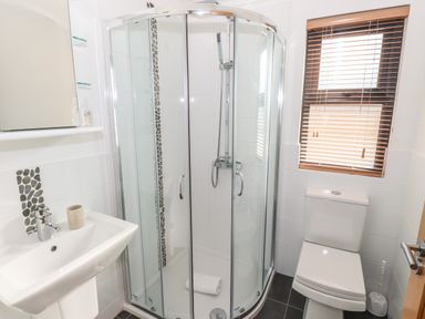 A bathroom with a corner shower enclosure a sink a toilet and a window with blinds at Windermere Lodge in Bowness-On-Windermere