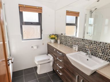 A bathroom with a toilet a sink on a wooden vanity with stone backsplash and a window with blinds at Windermere Lodge in Bowness-On-Windermere