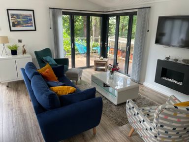 A living room with blue and patterned chairs a white coffee table and a wall-mounted tv at Windermere Lodge in Bowness-On-Windermere