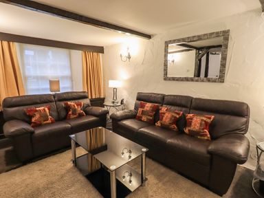 A living room with two brown leather sofas a glass coffee table pillows wall mirror lamps and orange curtains at Birchcroft Ambleside