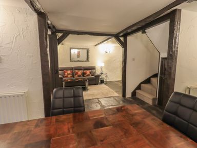 A dining table with black chairs and a living area with a sofa and pillows and stairs in a room with exposed beams at Birchcroft in Ambleside