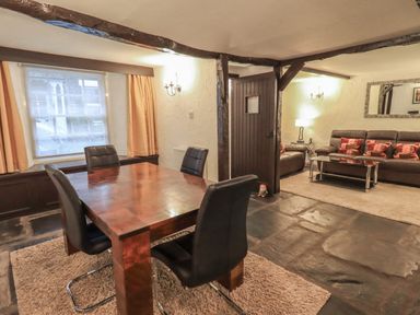 A dining area with a wooden table and four black chairs next to a living room with two brown sofas and a glass coffee table at Birchcroft in Ambleside