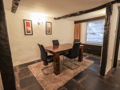 A dining room with a wooden table and four black chairs on a rug near a window at Birchcroft in Ambleside