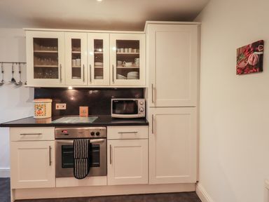 A kitchen with white cabinets glass doors showing dishes oven microwave and utensil rack at Birchcroft Ambleside