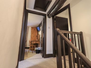 A hallway with carpeted floor leading to rooms with wooden furniture and a television at Birchcroft Ambleside