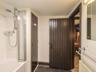 A bathroom with a bathtub and shower head dark wooden doors and a towel rail at Birchcroft in Ambleside