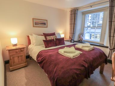A bedroom with a double bed with pillows and folded towels on a burgundy blanket with wooden nightstands and lamps at Birchcroft in Ambleside