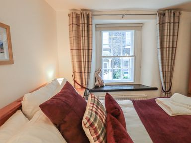 A bedroom with a window with plaid curtains and a bed with pillows and folded towels at Birchcroft Ambleside