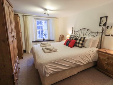 A bedroom with a double bed with towels on it a window with curtains wooden wardrobes and bedside tables at Birchcroft Ambleside