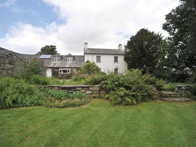 A stone house with a garden and lawn with stone steps and plants at Robin Cottage in Troutbeck
