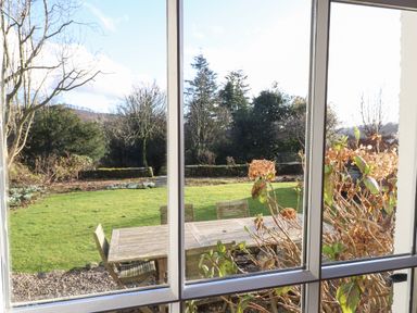 A garden with a wooden table and chairs viewed through a window at Robin Cottage in Troutbeck