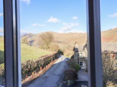 A road with hedges and houses beside hills seen through a window at Robin Cottage in Troutbeck