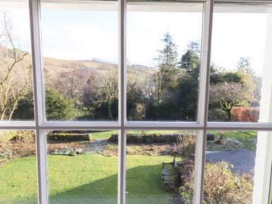 A garden with grass trees a bench and hills in the background as seen through a window at Robin Cottage in Troutbeck