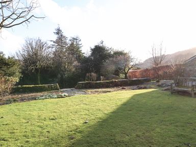 A grassy garden area with trees stone walls and a wooden bench at Robin Cottage in Troutbeck